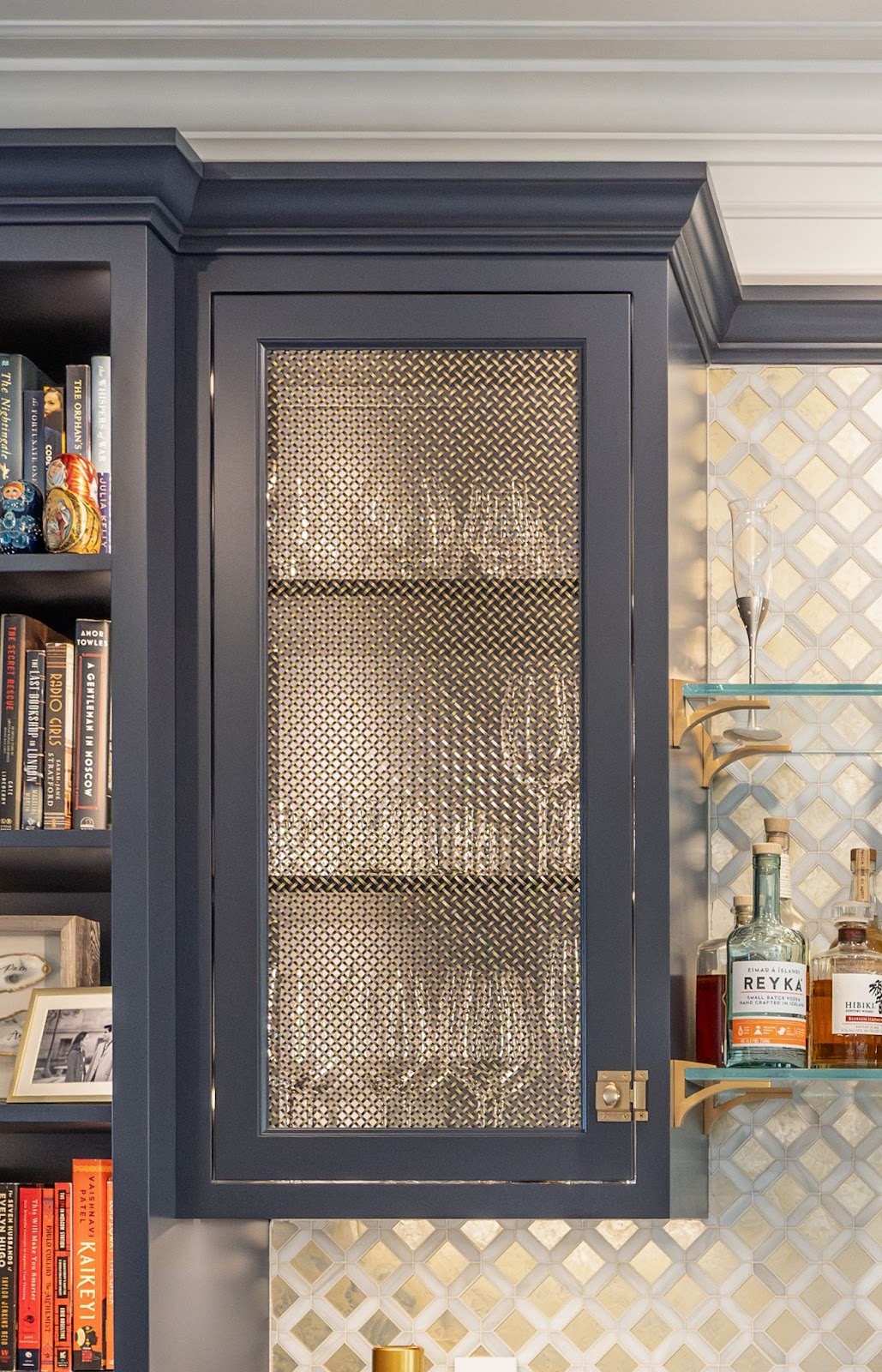 Closeup of a navy cabinet with mesh inlay by Laslo Custom Kitchens Books to the left and alcohol to the right.