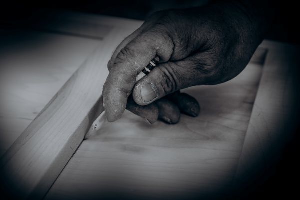 A closeup of a carpenter's hand holding a pencil and marking a piece of wood.