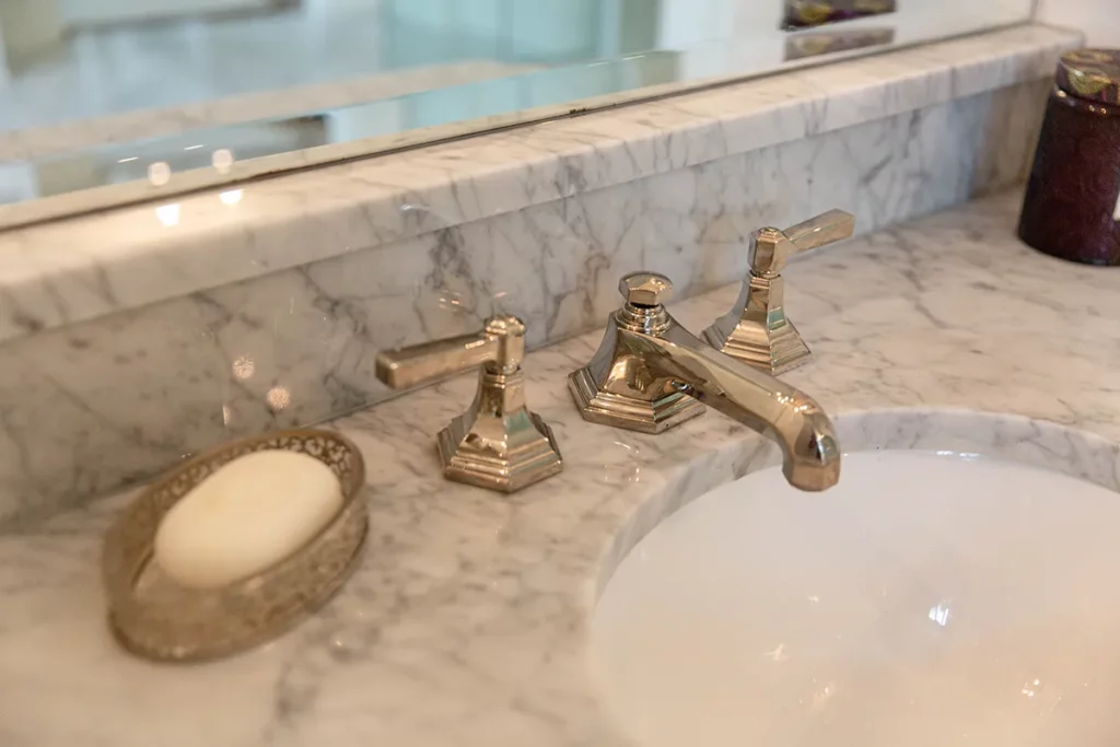 venetian style bathroom remodel with marble tile and marble sink with nickel faucet