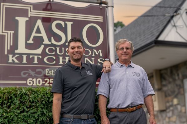 Two men stand in front of a brown Laslo Custom Kitchens sign in Pennsylvania.