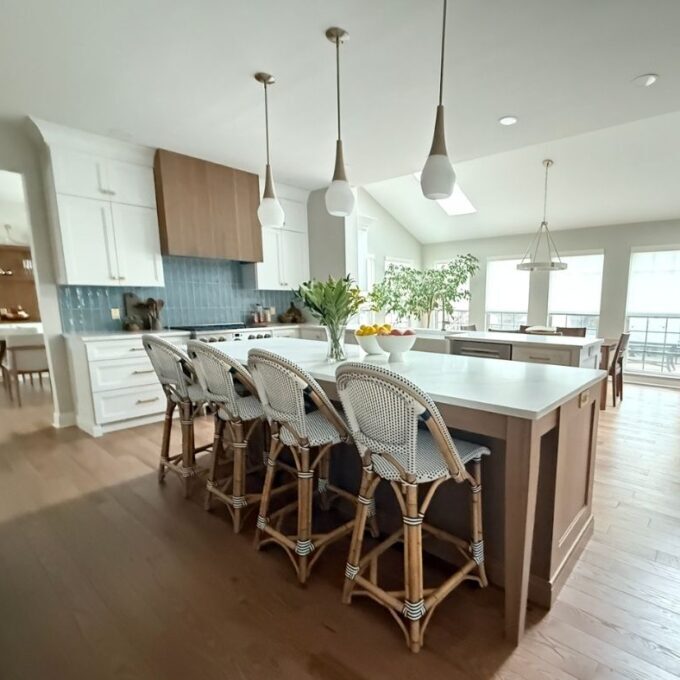 A kitchen with a large island, 4 white French barstools, and 3 lights.