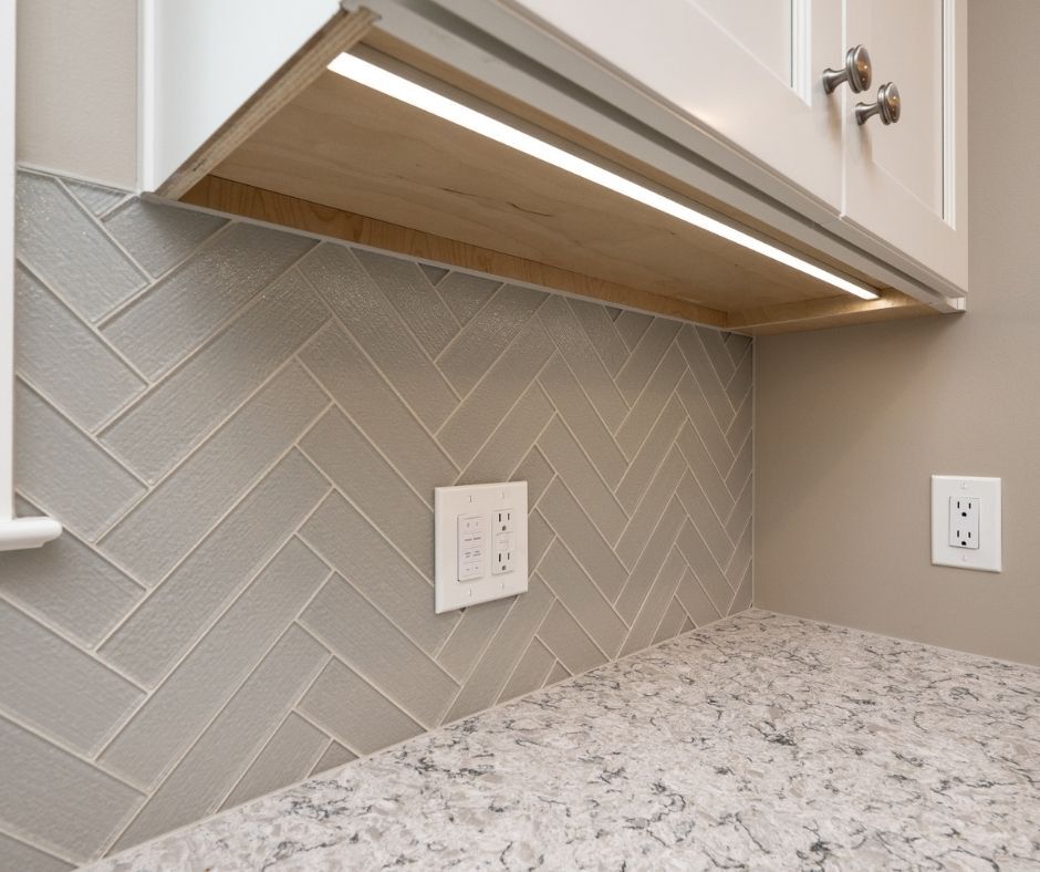Under cabinet strip lights above a white kitchen counter and light gray backsplash.