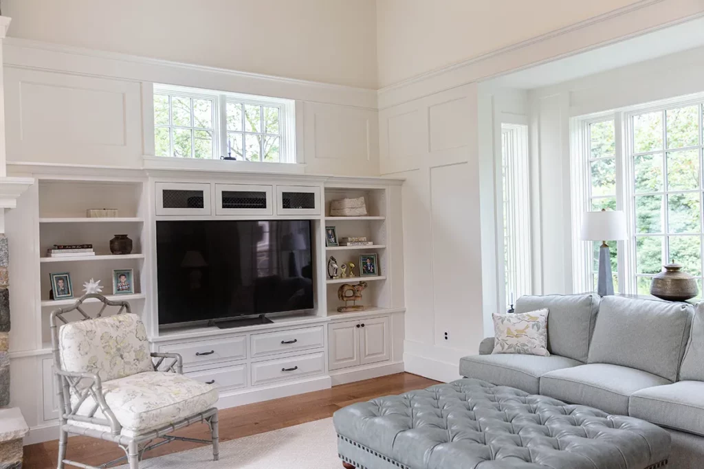 Custom cabinetry that is white and is used as an entertainment center with a leather Ottoman and couch.