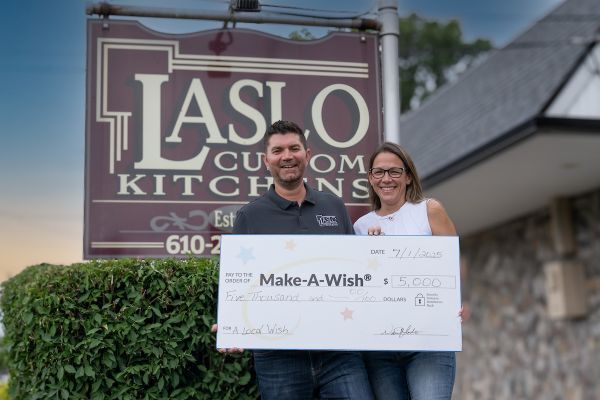 A man and a woman stand in front of Laslo Custom Kitchens with a large check for Make-A-Wish.
