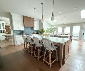 A kitchen with a large island, 4 white French barstools, and 3 lights.