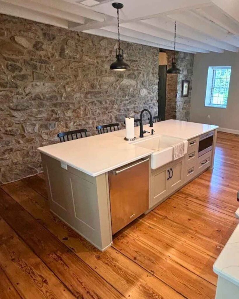 A white island in a farmhouse kitchen next to a gray stone wall.