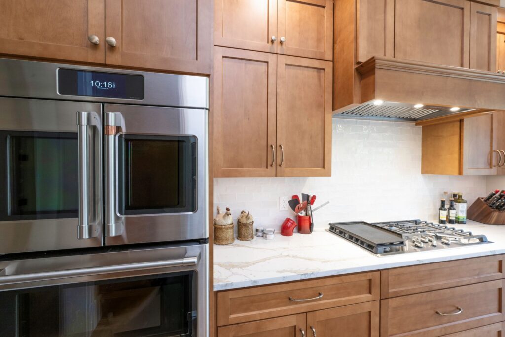 A close-up view of integrated double wall ovens nestled into hard maple kitchen cabinetry with a smooth dull finish.