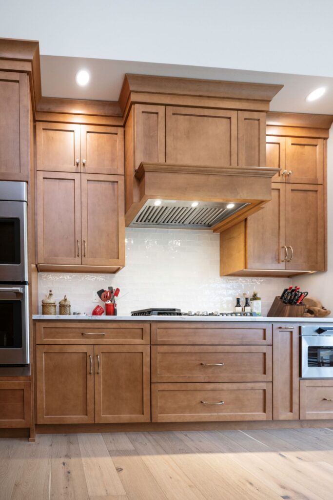 A vertical view of a custom wood range hood featuring precise stacked large cove and flat stock crown molding running to the ceiling.