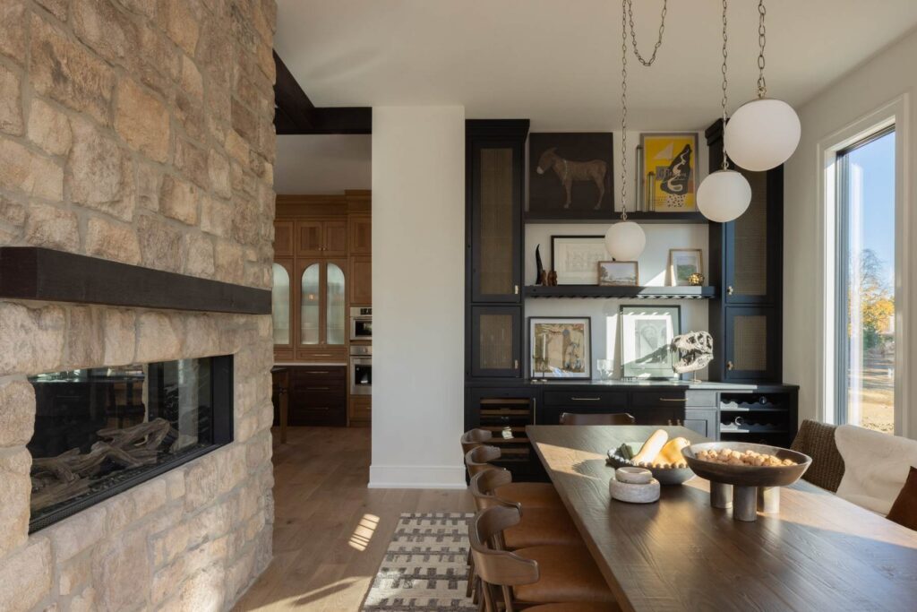 Open dining area with dark built-in cabinetry, globe pendants, and a two-sided stone fireplace.