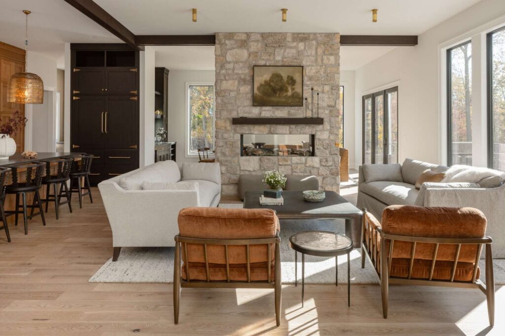 Living room view toward the mixed-wood kitchen with stone fireplace, dark beams, and wide-plank flooring.