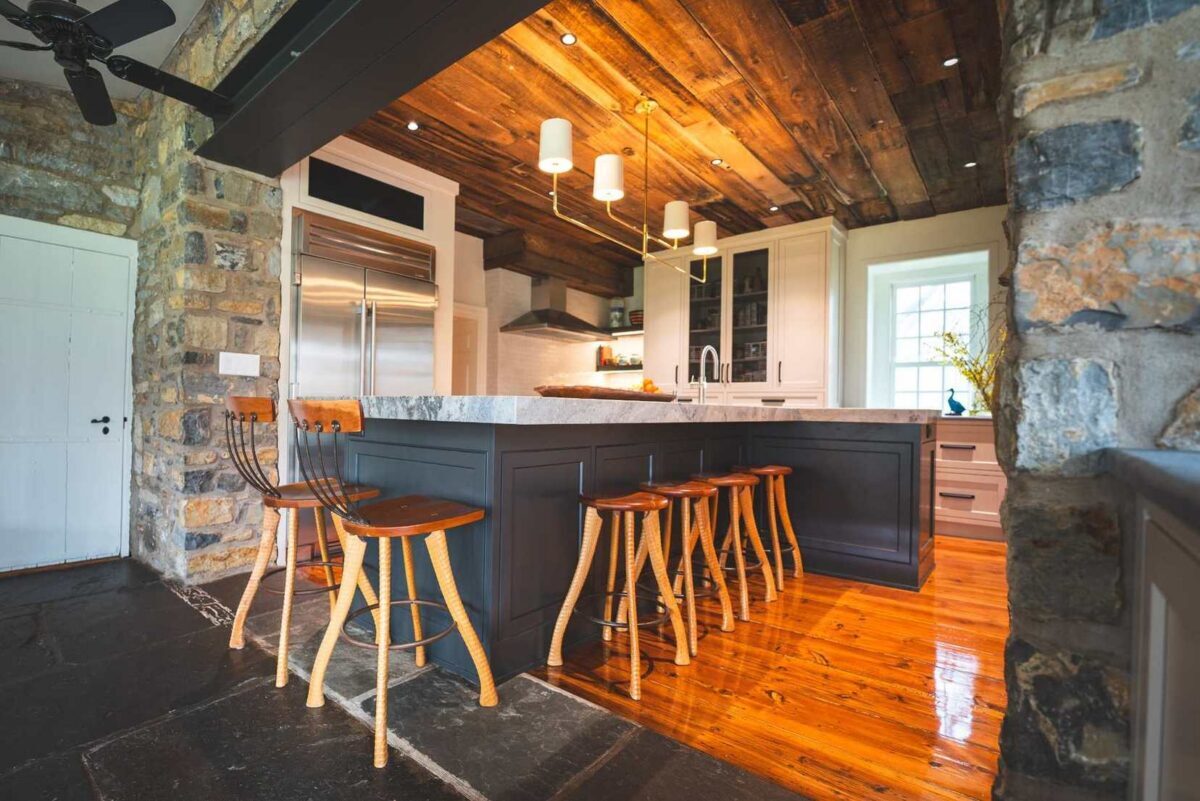 Architectural kitchen design in Allentown with a dark center island, exposed stone walls, and a vaulted wood ceiling, designed by Swine Design, LLC.
