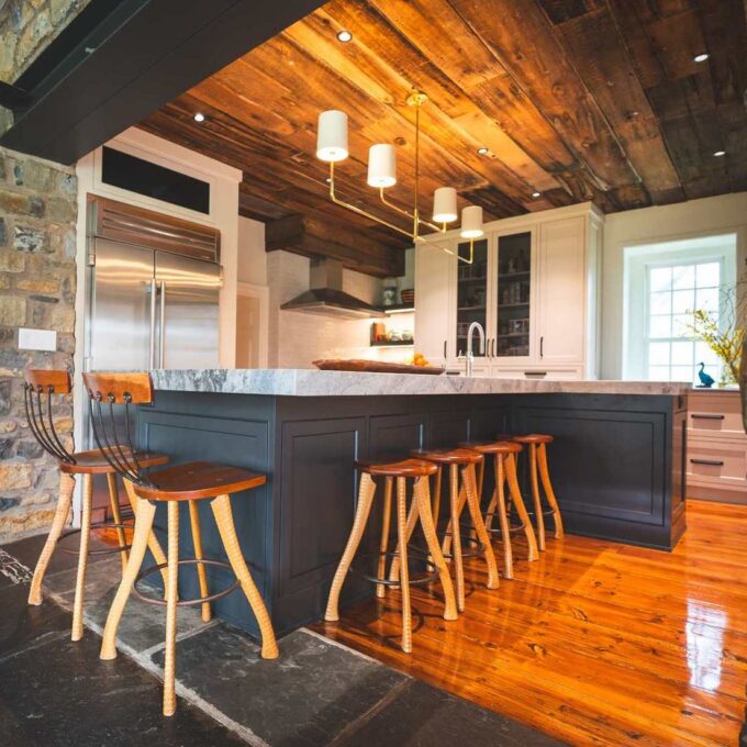 Architectural kitchen design in Allentown with a dark center island, exposed stone walls, and a vaulted wood ceiling, designed by Swine Design, LLC.