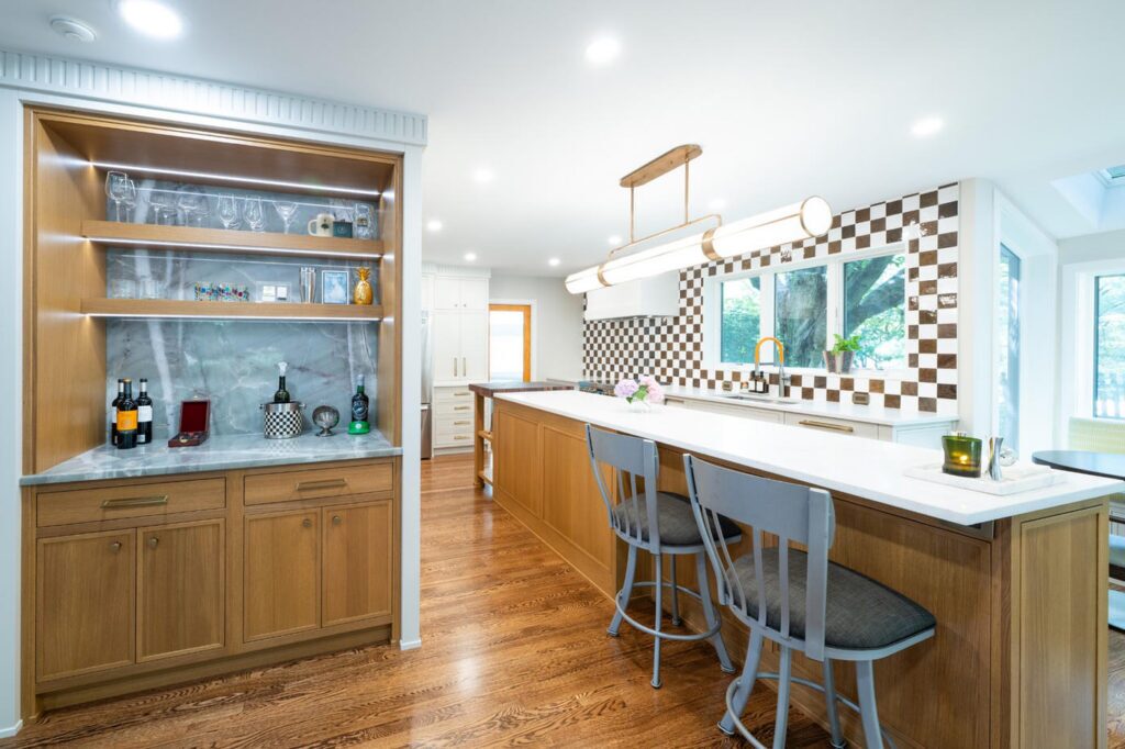 Rift cut white oak dry bar with glassware on floating shelves beside the matching kitchen island.