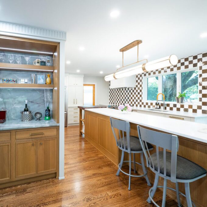 Rift cut white oak dry bar with glassware on floating shelves beside the matching kitchen island.
