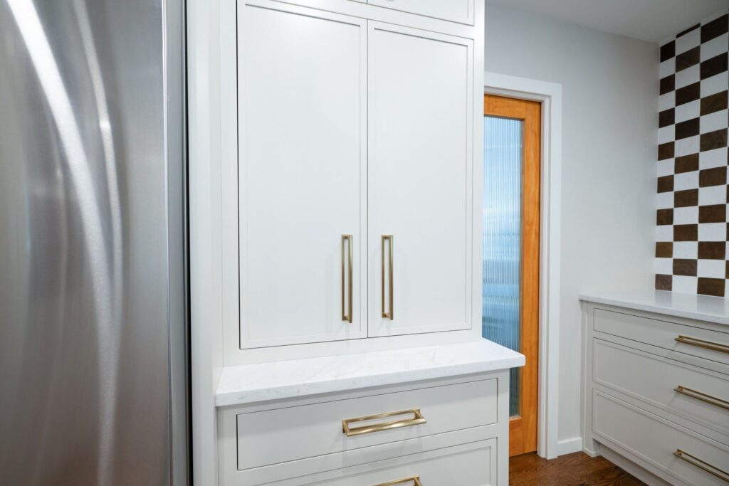 Closed taupe inset cabinet doors above a quartz counter and drawers beside the refrigerator.