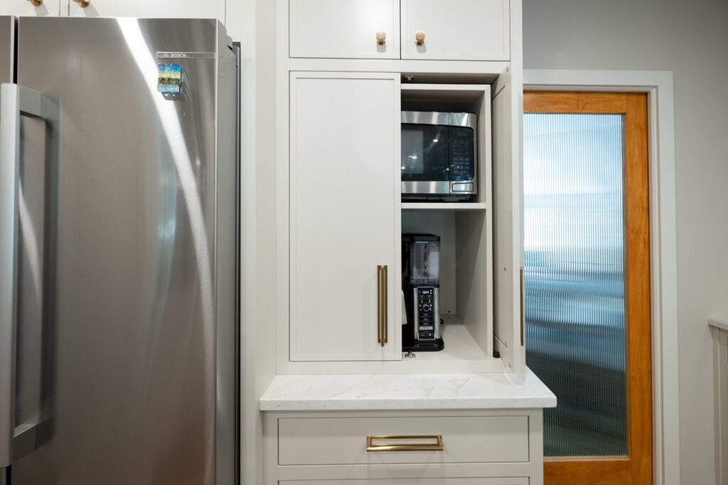 Partly open taupe cabinet doors reveal a microwave and coffee maker beside the refrigerator.