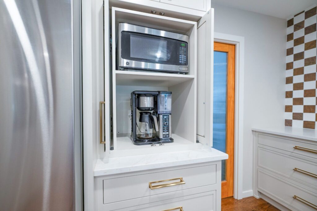 Open taupe kitchen cabinet beside the refrigerator with a concealed microwave and coffee maker.