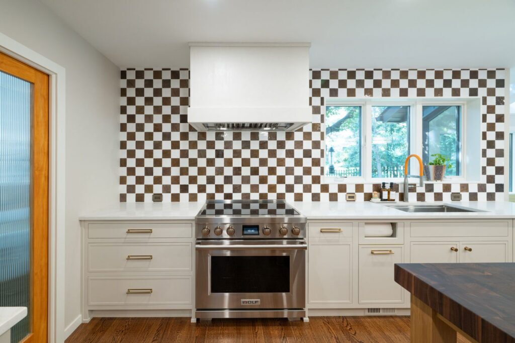 Wolf range between taupe inset drawer cabinets beneath a white hood and brown-and-white checkered backsplash.