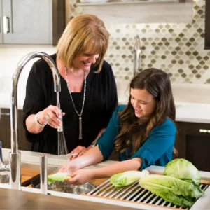 A woman with blonde hair and girl wash lettuce at a Galley Workstation installed by Laslo Custom Kitchens.